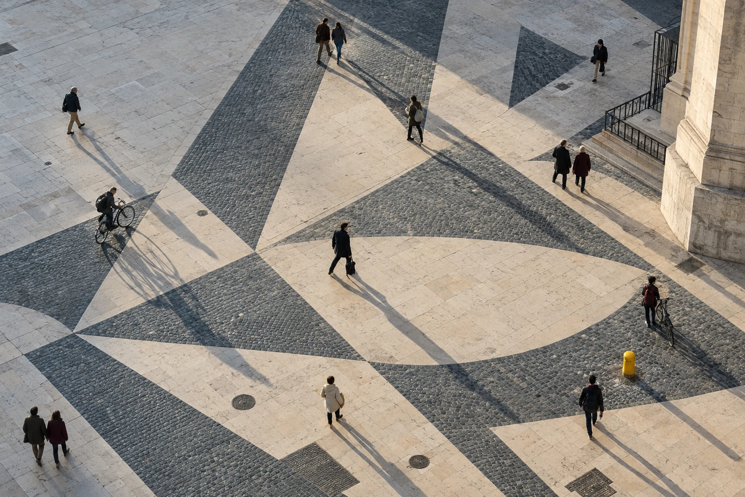 People crossing a geometric stone plaza in afternoon light.